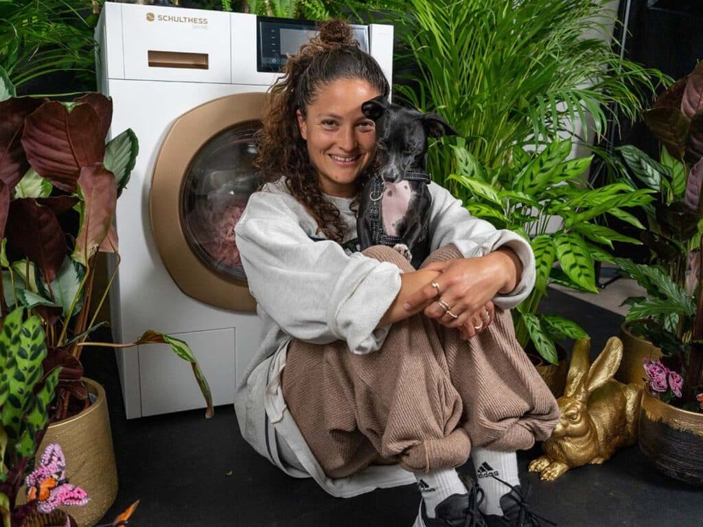 Frau mit Hund vor Waschmaschine und Pflanzen